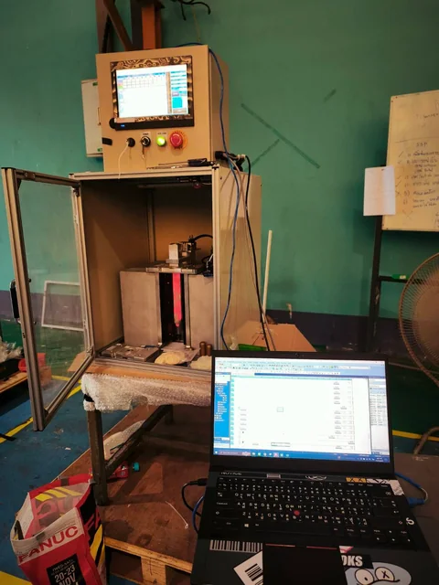 ชุดเครื่องจักรที่มีจอ HMI ด้านบน และคอมพิวเตอร์แสดงโปรแกรม PLC อยู่ด้านหน้า