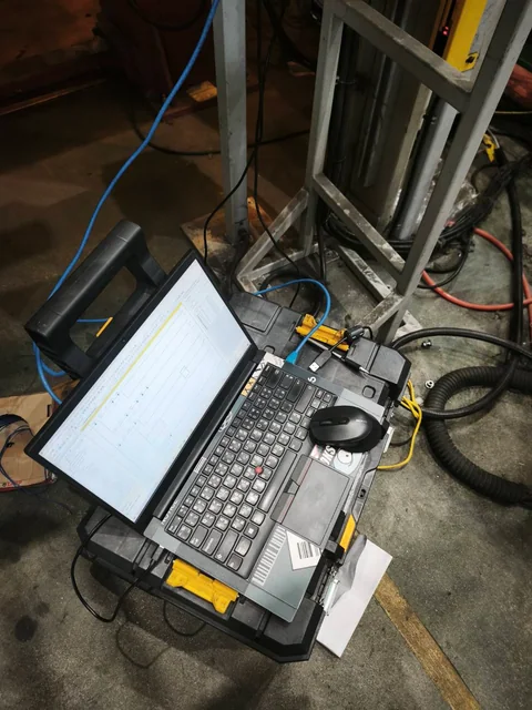 คอมพิวเตอร์แสดงโปรแกรม PLC วางบนกล่องเครื่องมือข้างโครงเครื่องจักร